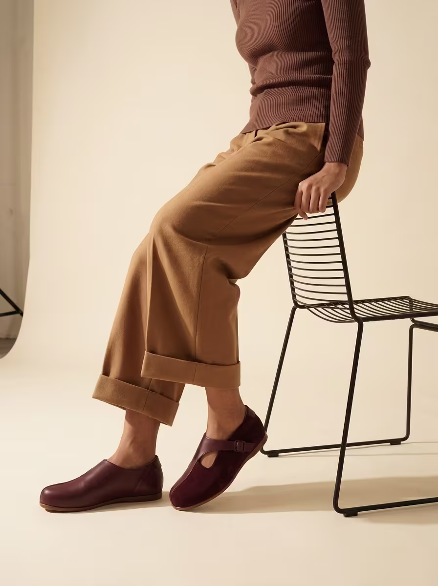 A woman seated in a cane chair wearing cream Kaalcari slip-ons
